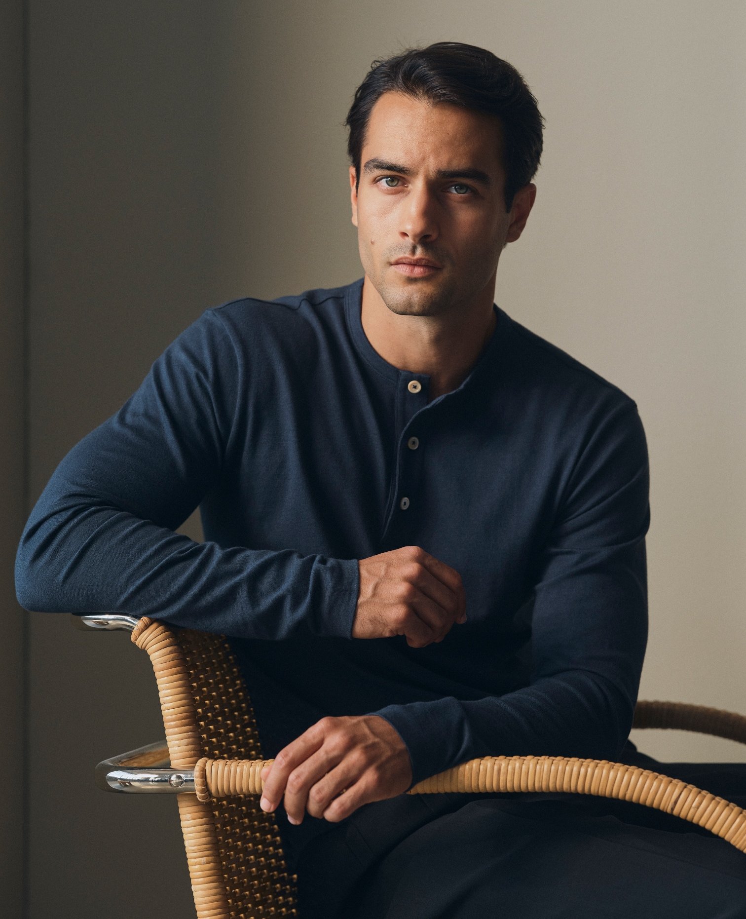 Model in a navy long-sleeve henley seated on a rattan chair