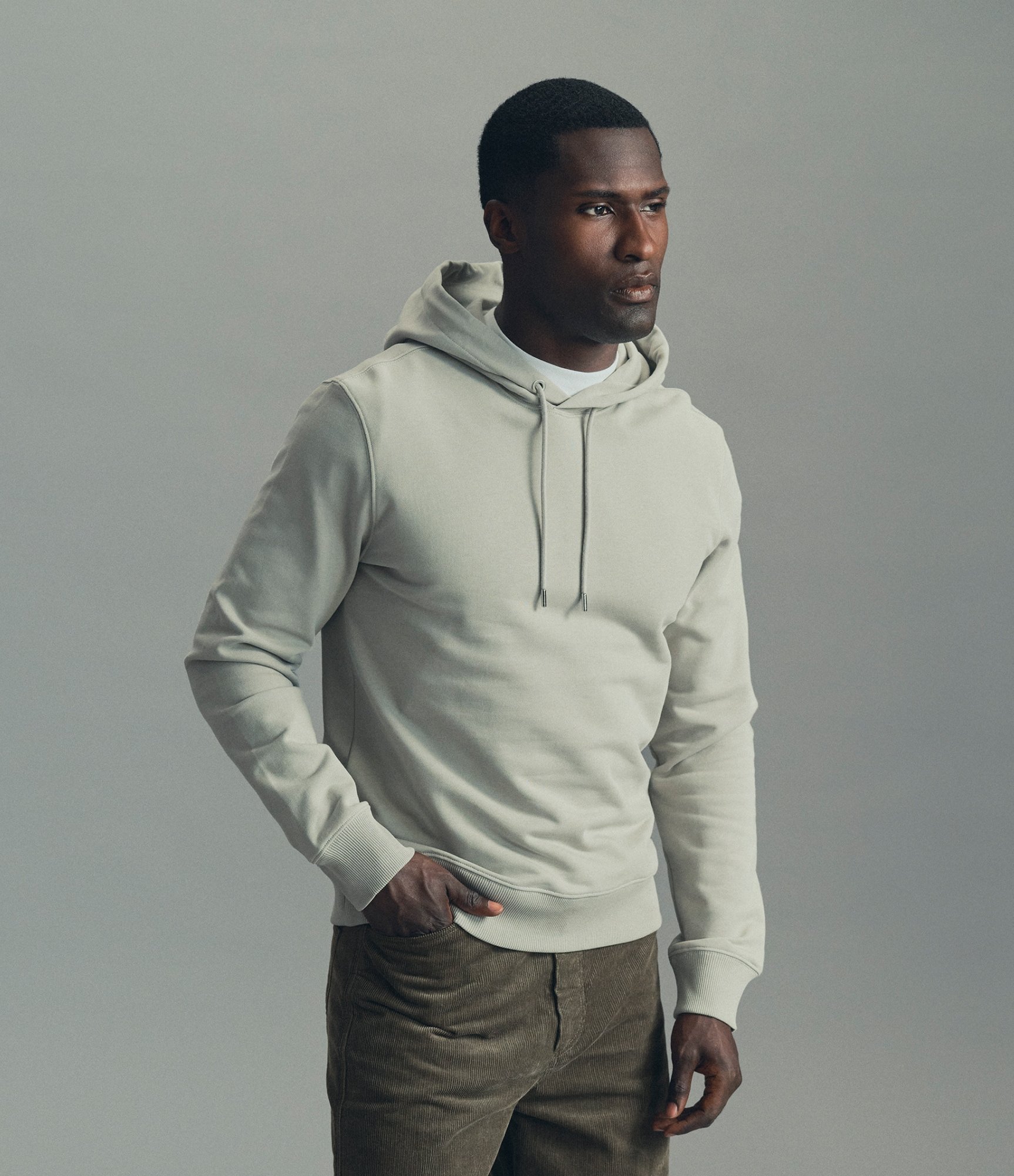 Model in a pale grey hoodie and olive trousers