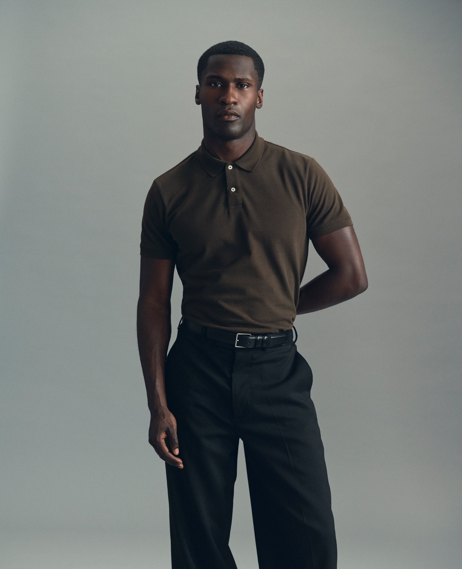 Model in a dark brown polo shirt and black trousers