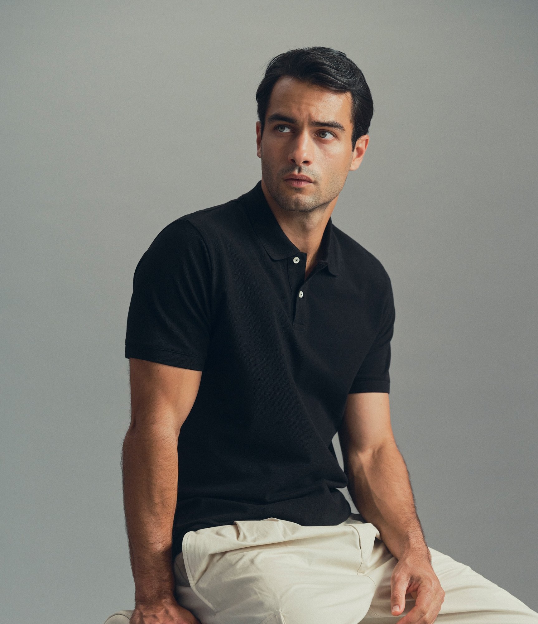 Model in a black polo shirt and cream trousers