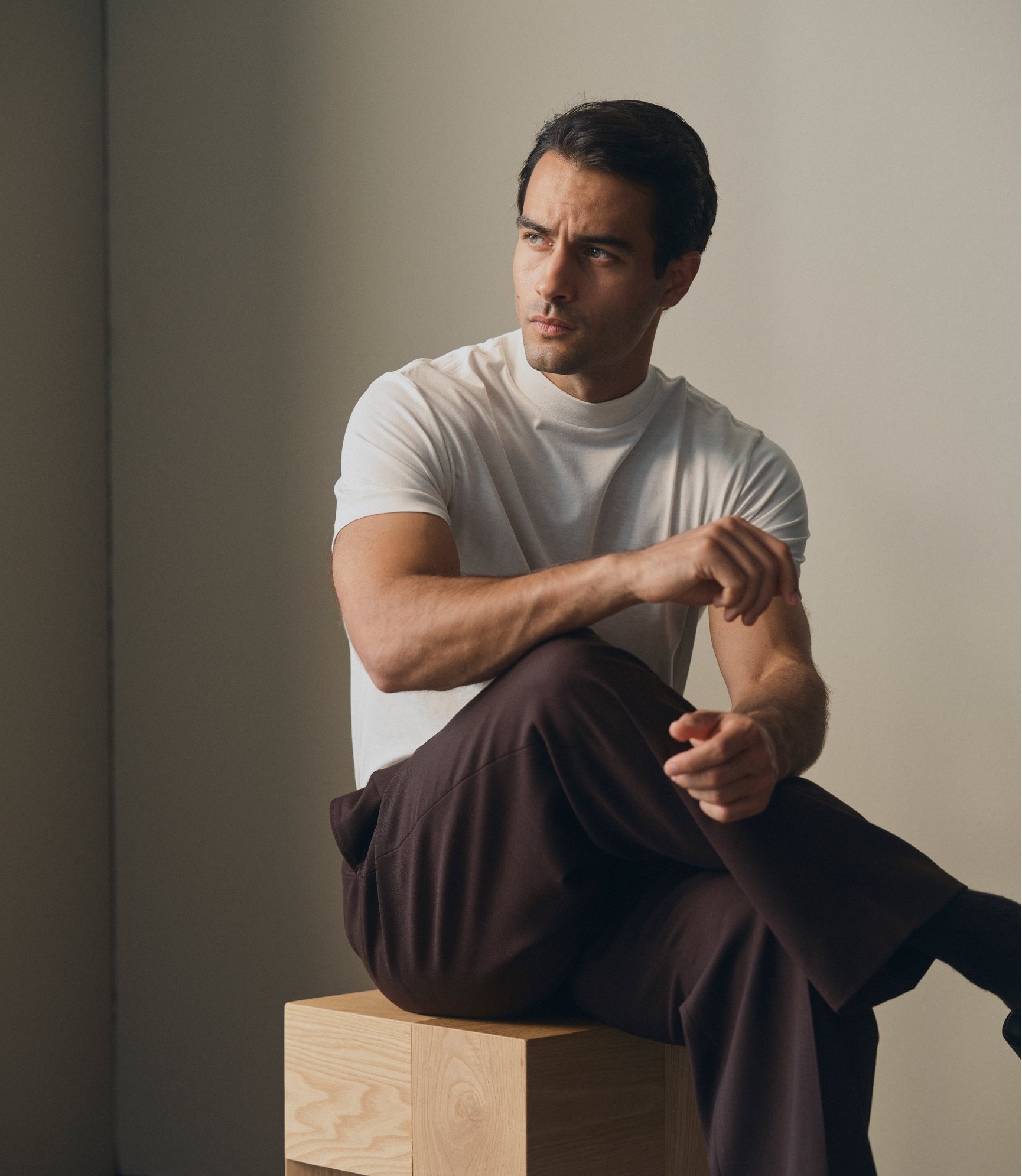 Model seated on a wooden block in a white T-Shirt and dark brown trousers