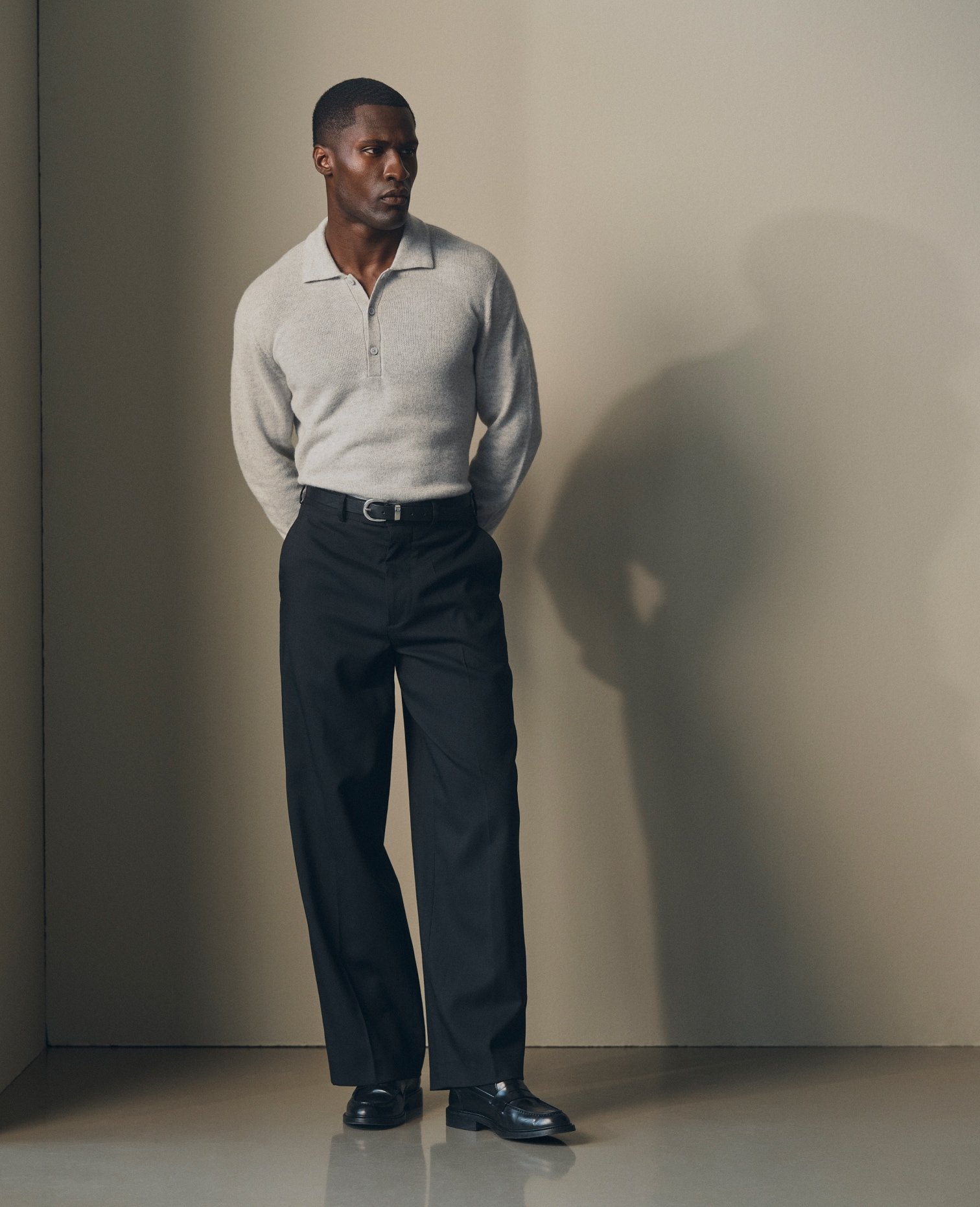 Model in a grey knitted polo and dark tailored trousers