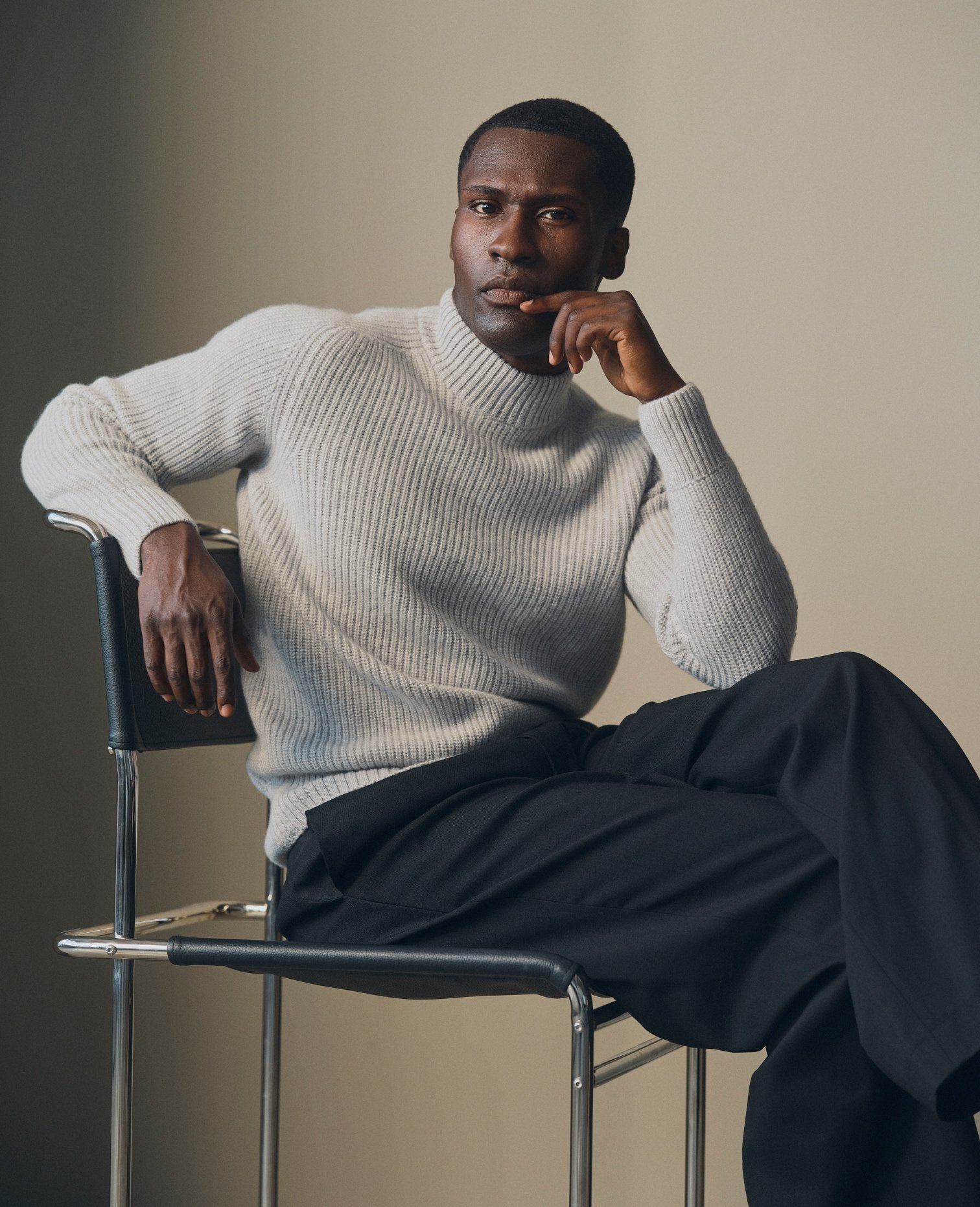 Model in a cream turtleneck seated on a chair