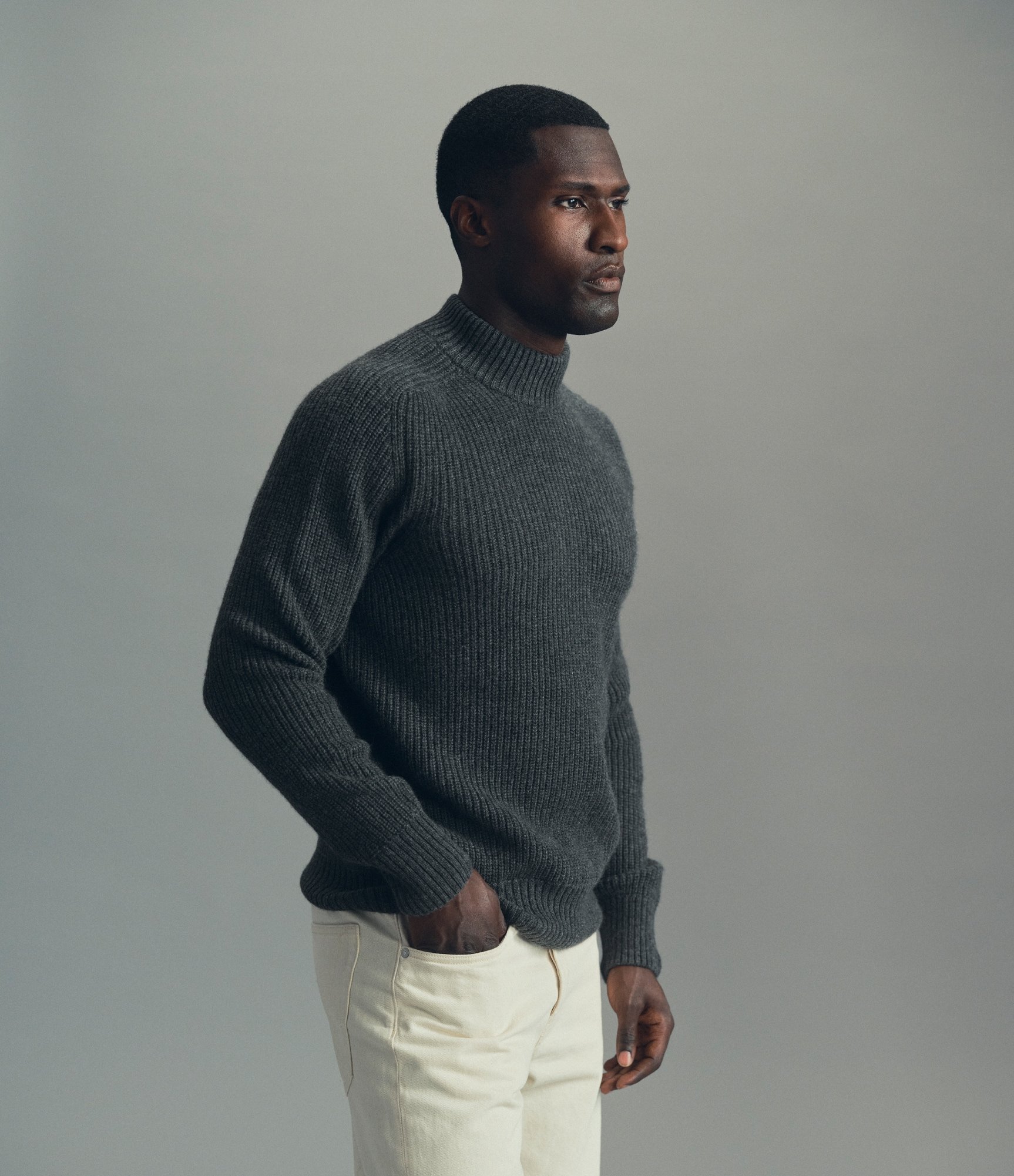 Model in a dark grey ribbed turtleneck and off-white trousers