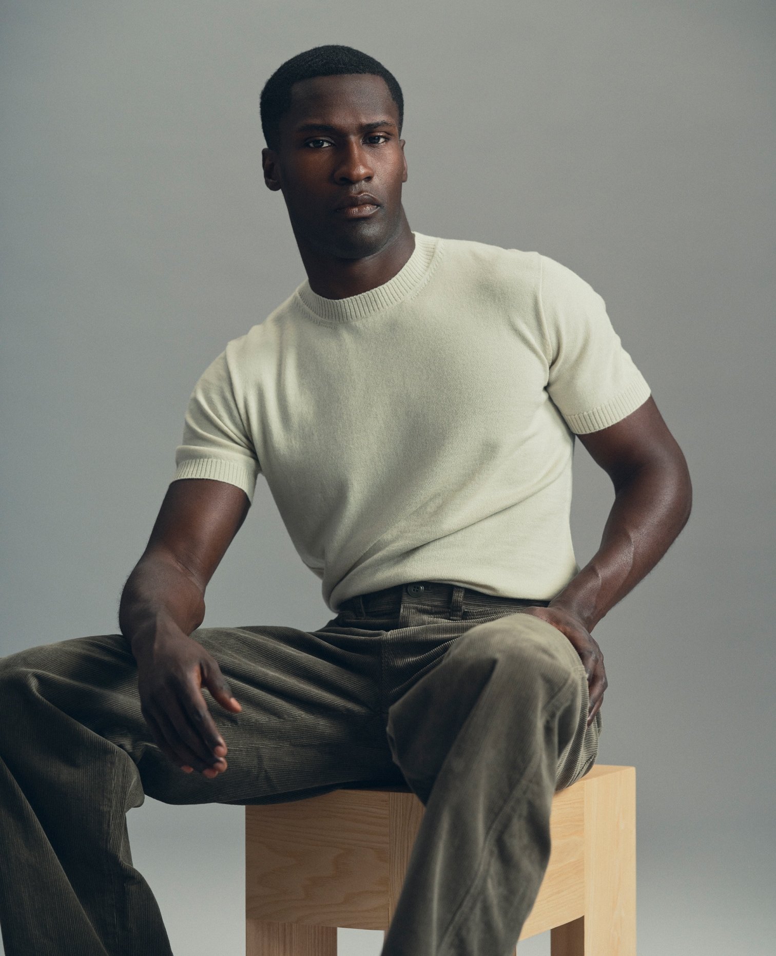 Model in a cream T-Shirt and olive trousers, seated