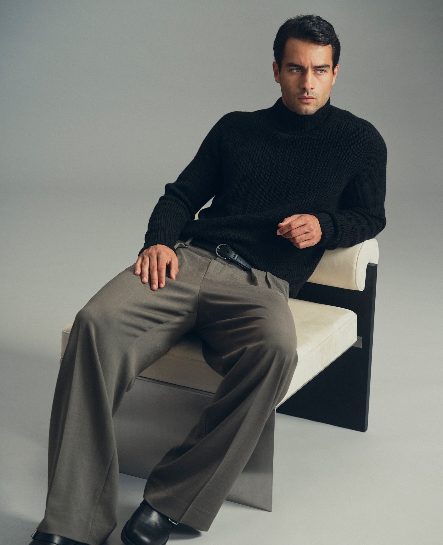 Model in a black turtleneck and grey wide-leg trousers, seated