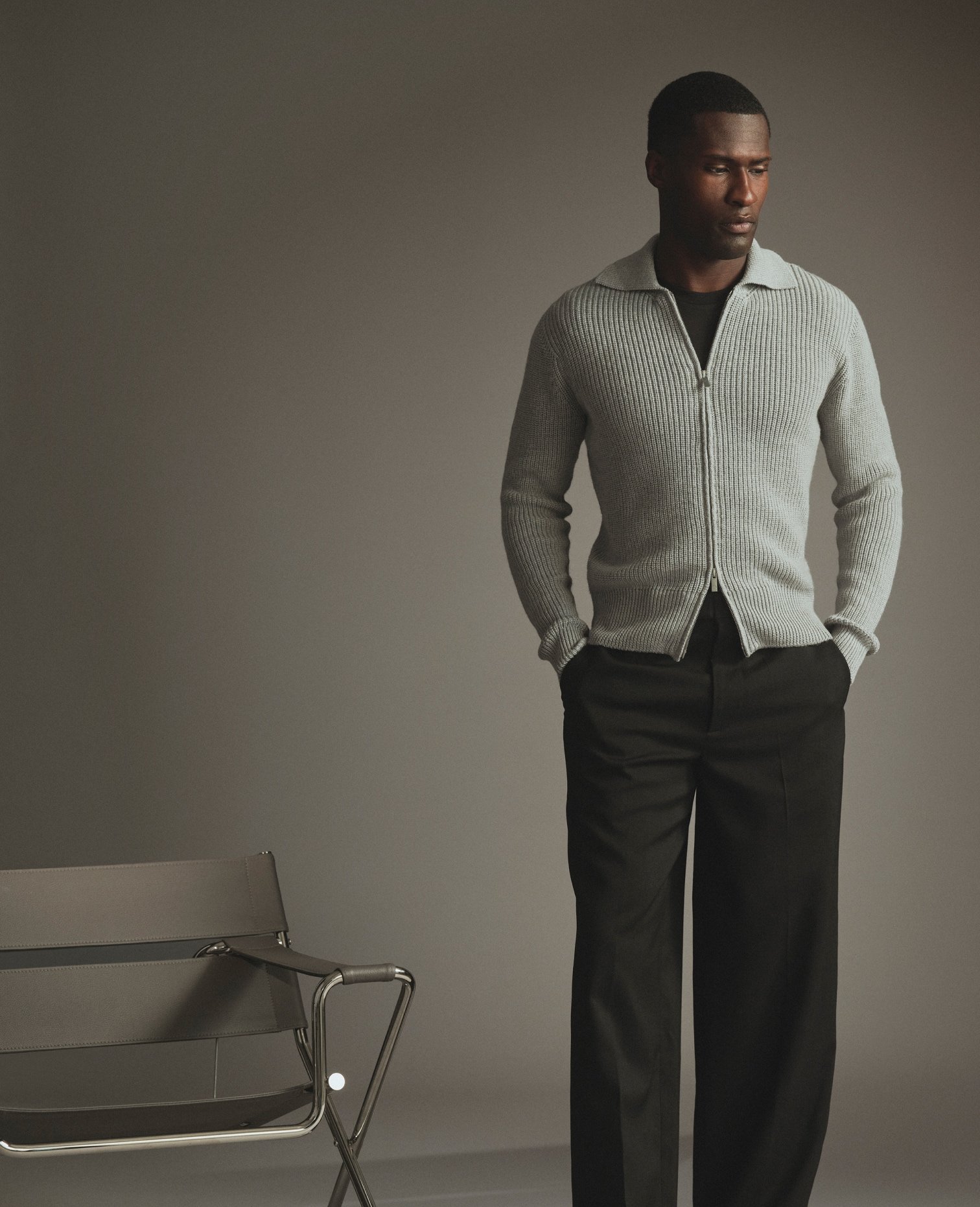 Model in a grey zip cardigan and dark trousers