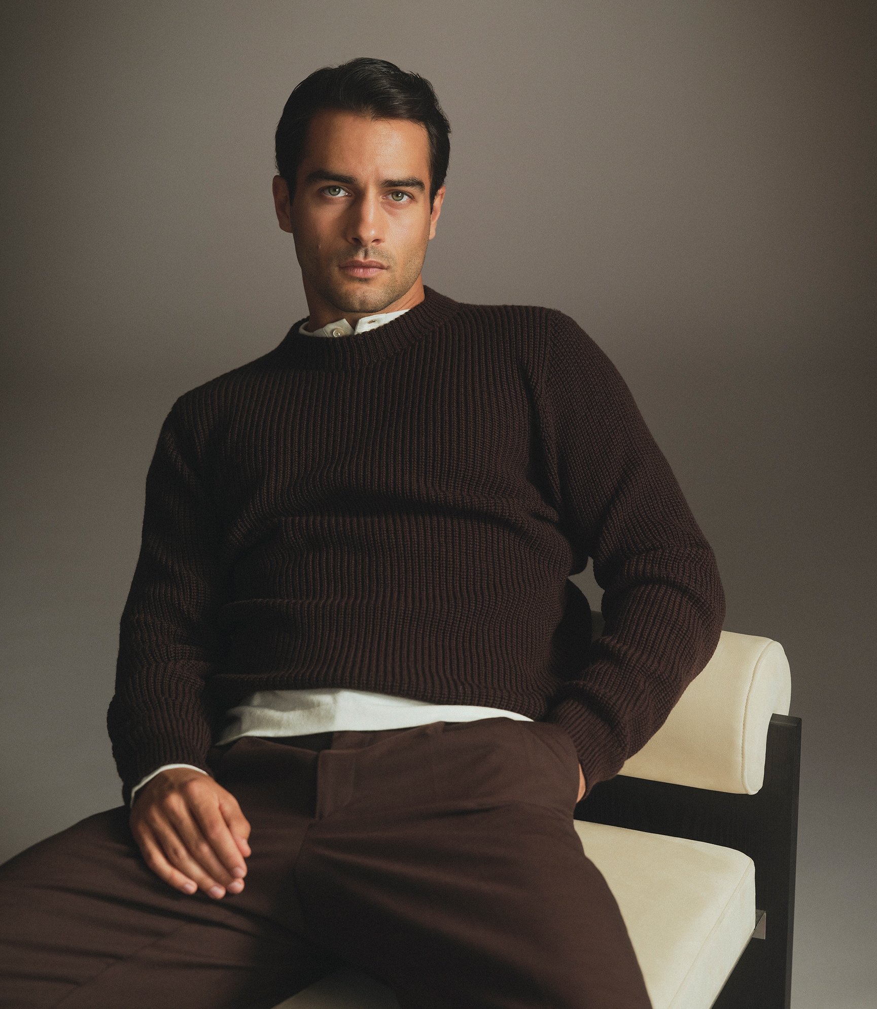 Model in a dark brown ribbed sweater and brown trousers, seated