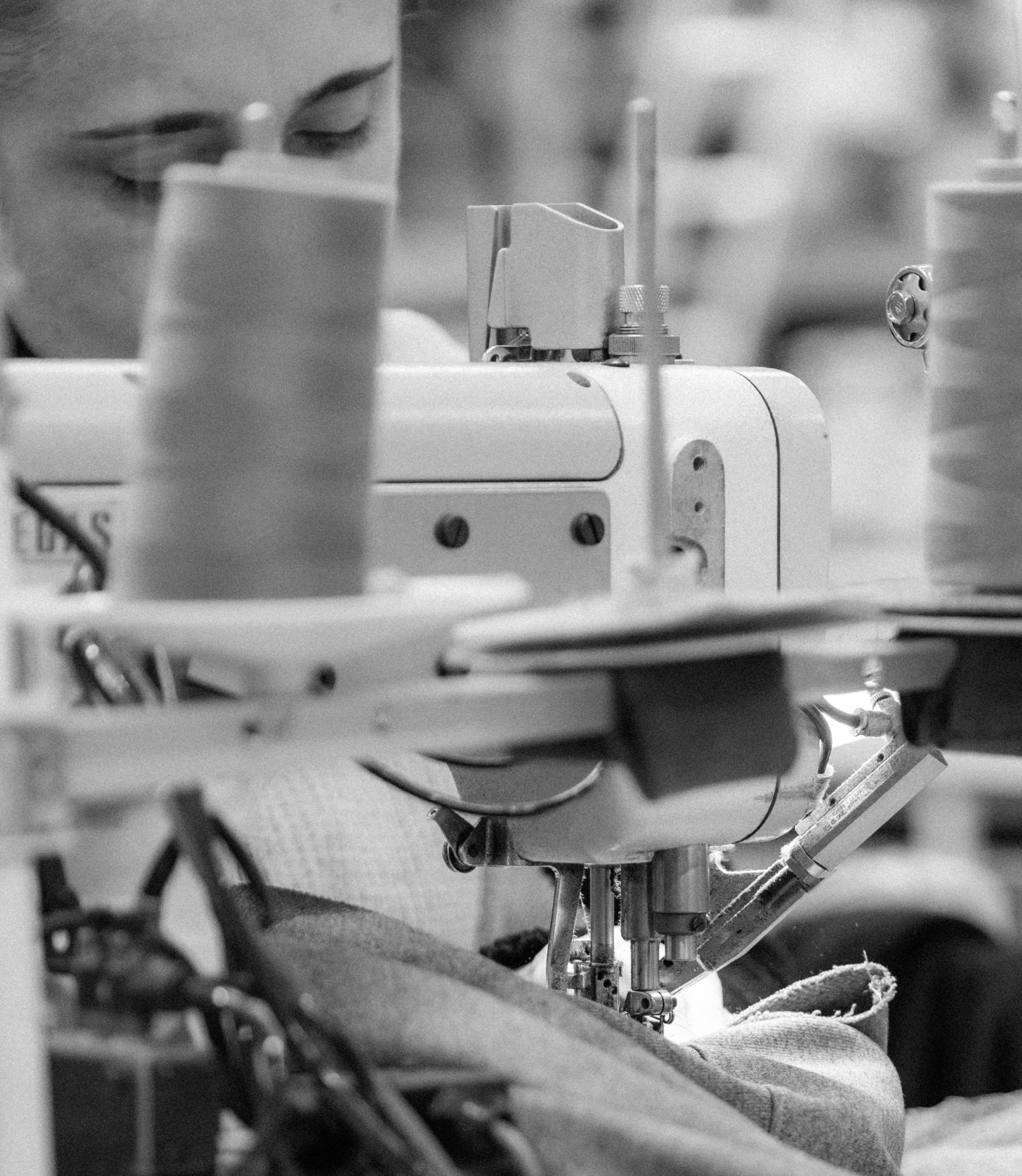 Thread cones above an industrial sewing machine in black and white