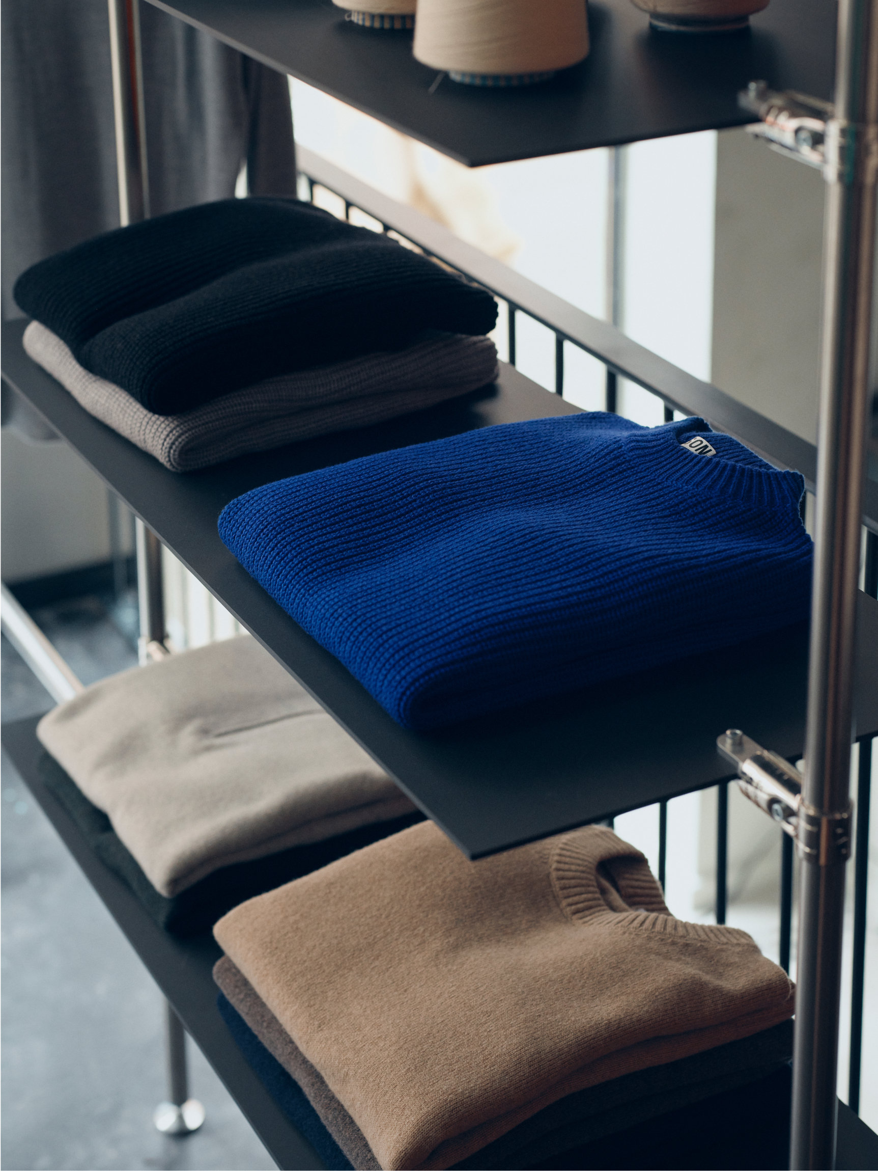 Folded knit sweaters in blue, gray, and brown on store display shelves