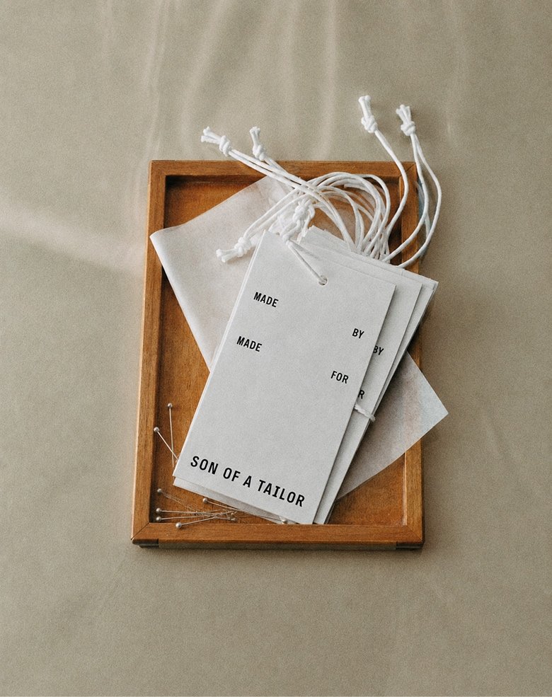 Son of a Tailor garment tags and drawstring bags on a wooden tray