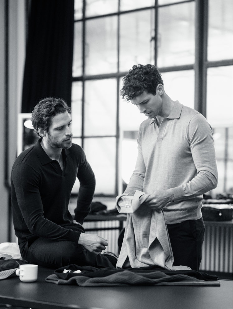 Two of the team inspecting knitted polo shirts laid out on a worktable in the studio