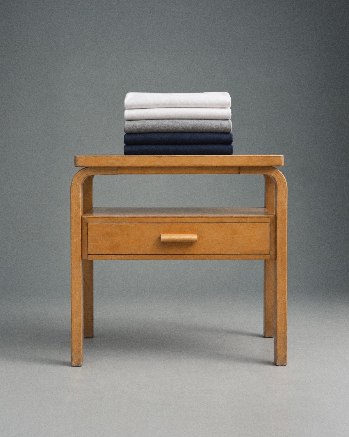 Folded T-shirts in white, grey and navy stacked on a wooden side table