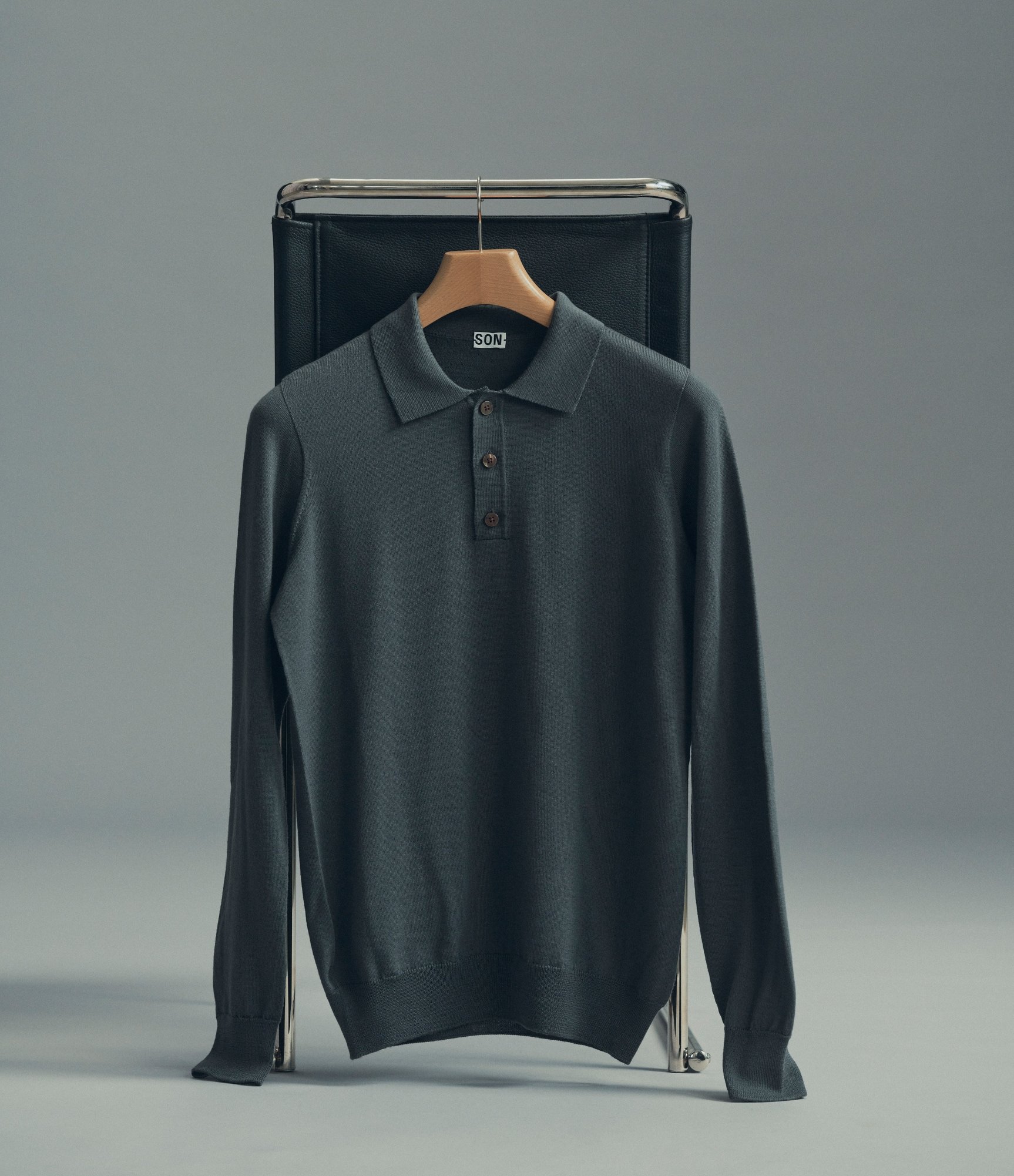 Our merino polo pullover in dark shadow hanging from a chair
