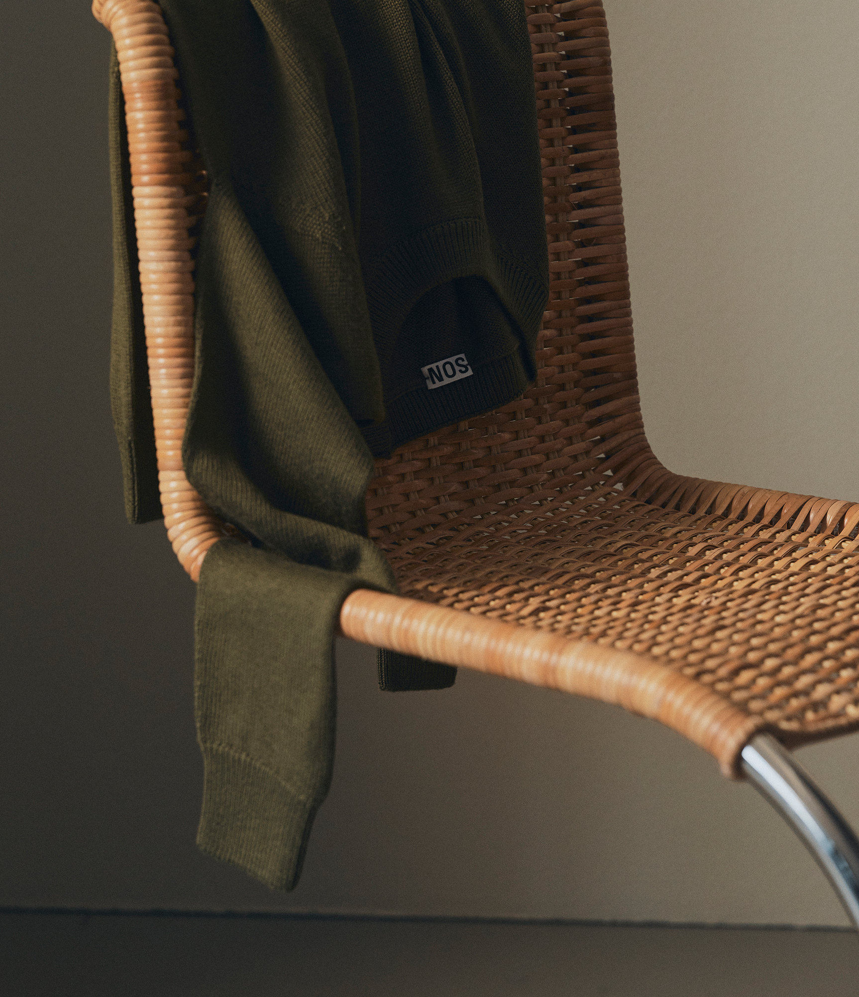 Our merino sweater in deep olive over a chair
