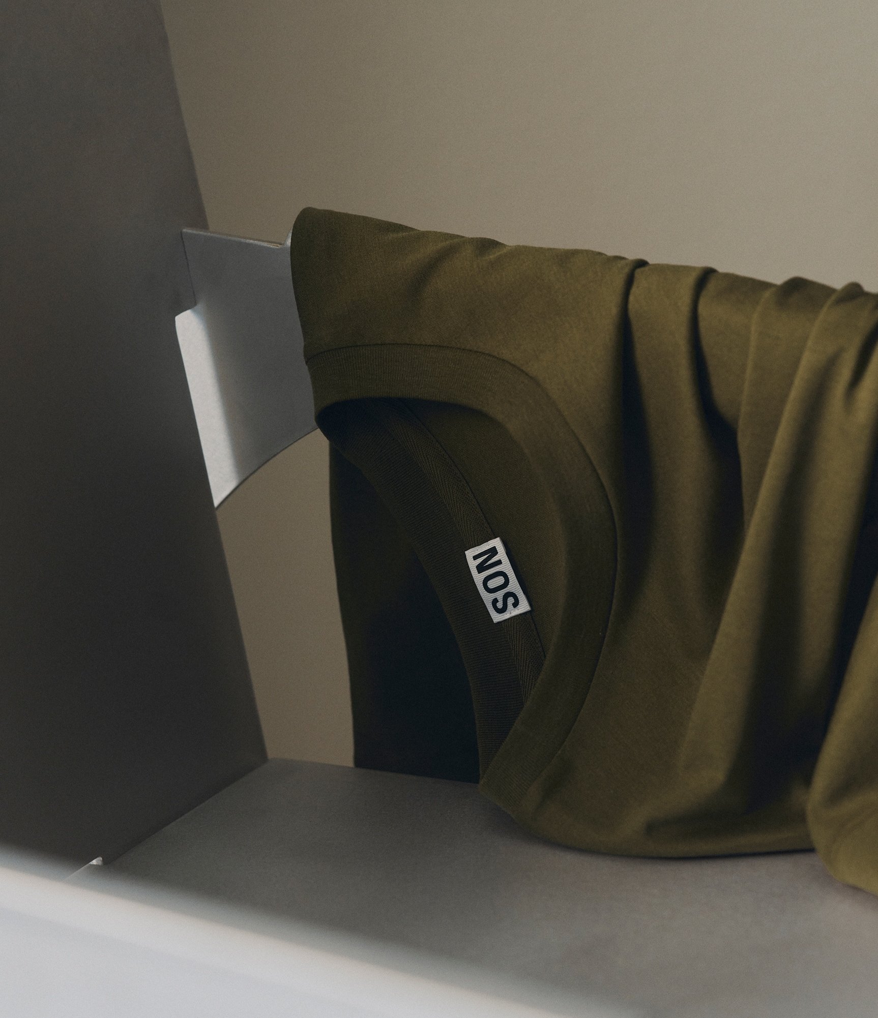 Silk T-Shirt in Dark Olive hanging off a chair