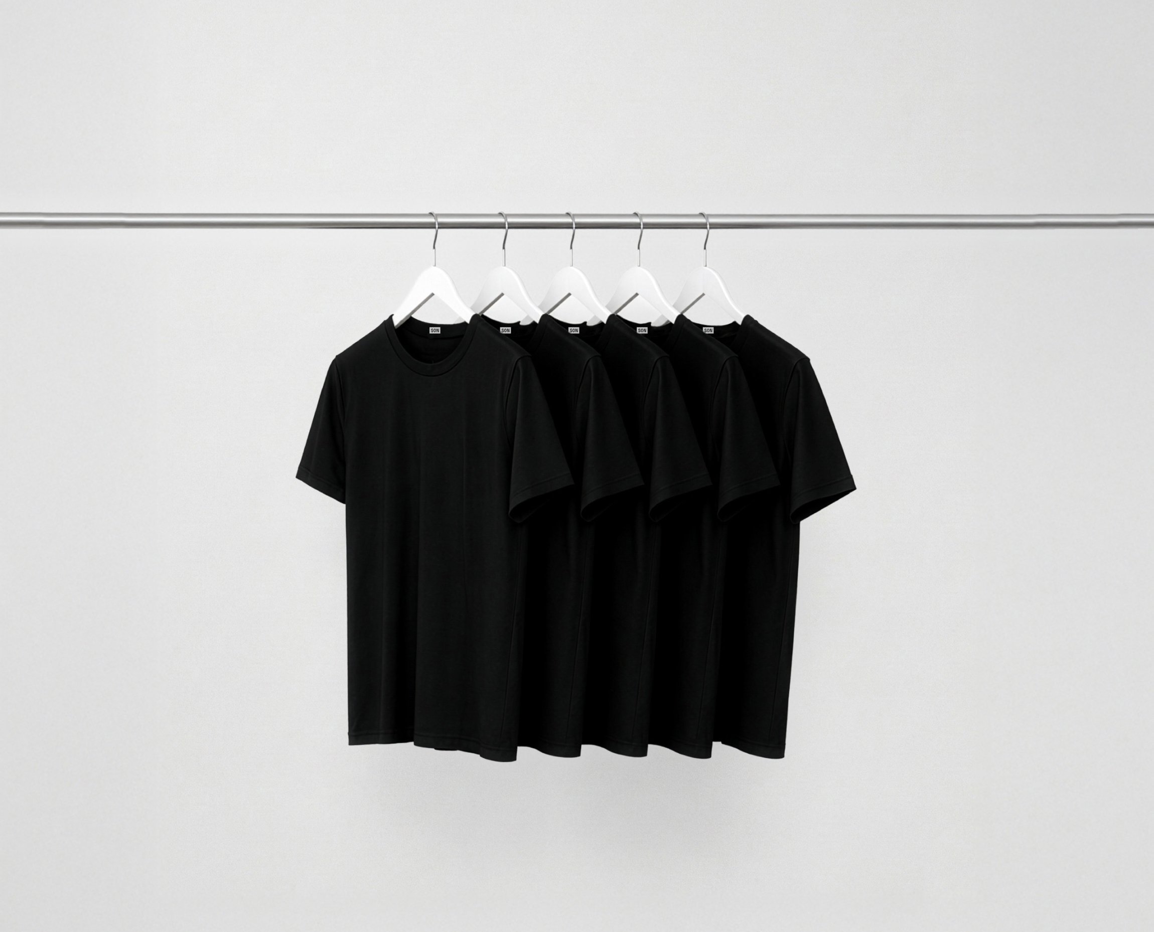 Black essentials bundle t-shirts hanging on a rack against a grey background